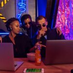 Three people collaborate on laptops in a cyber-themed workspace, discussing strategies.